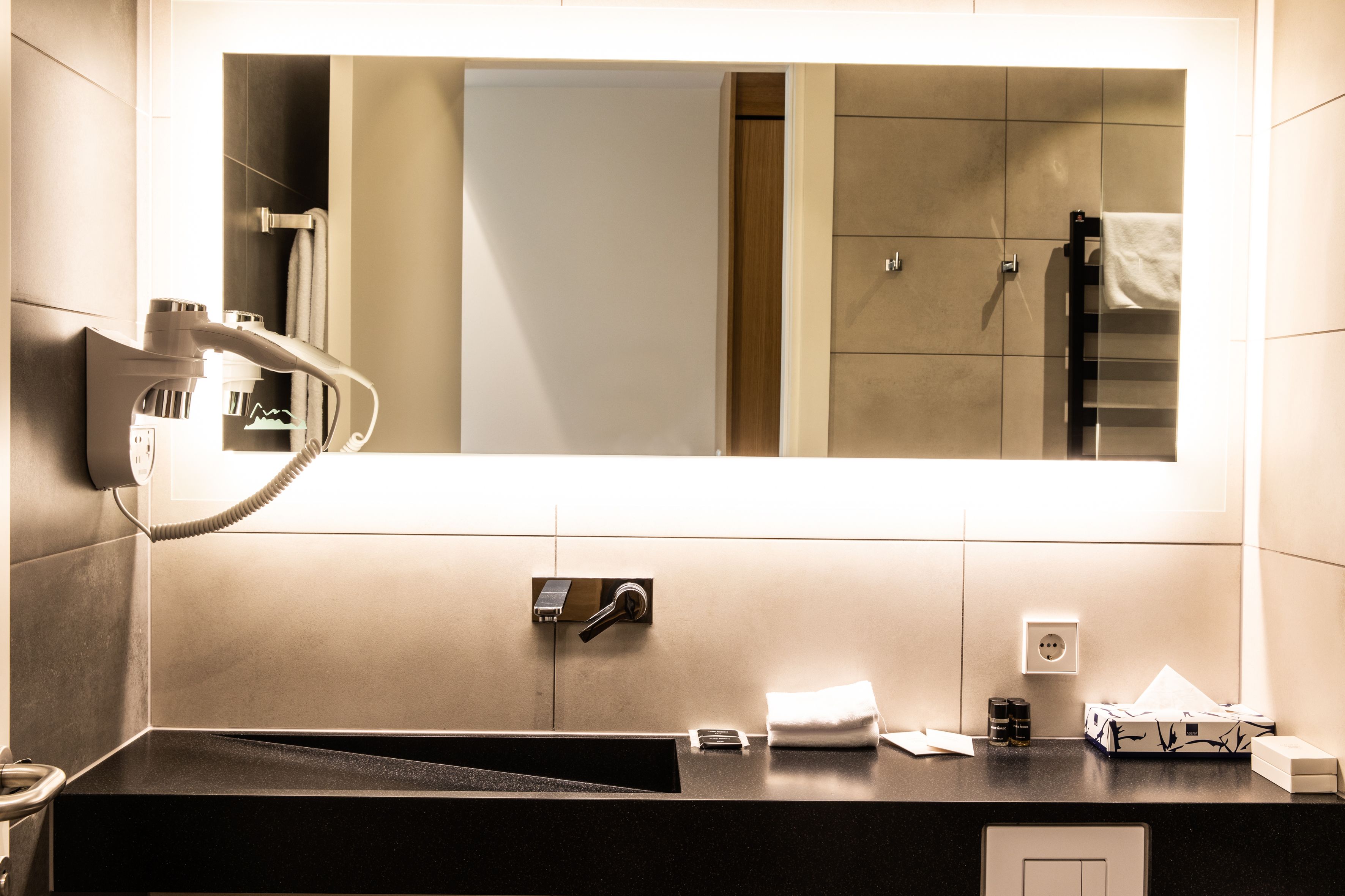 A modern bathroom with a large mirror, a towel rack, a sink, and a toilet.