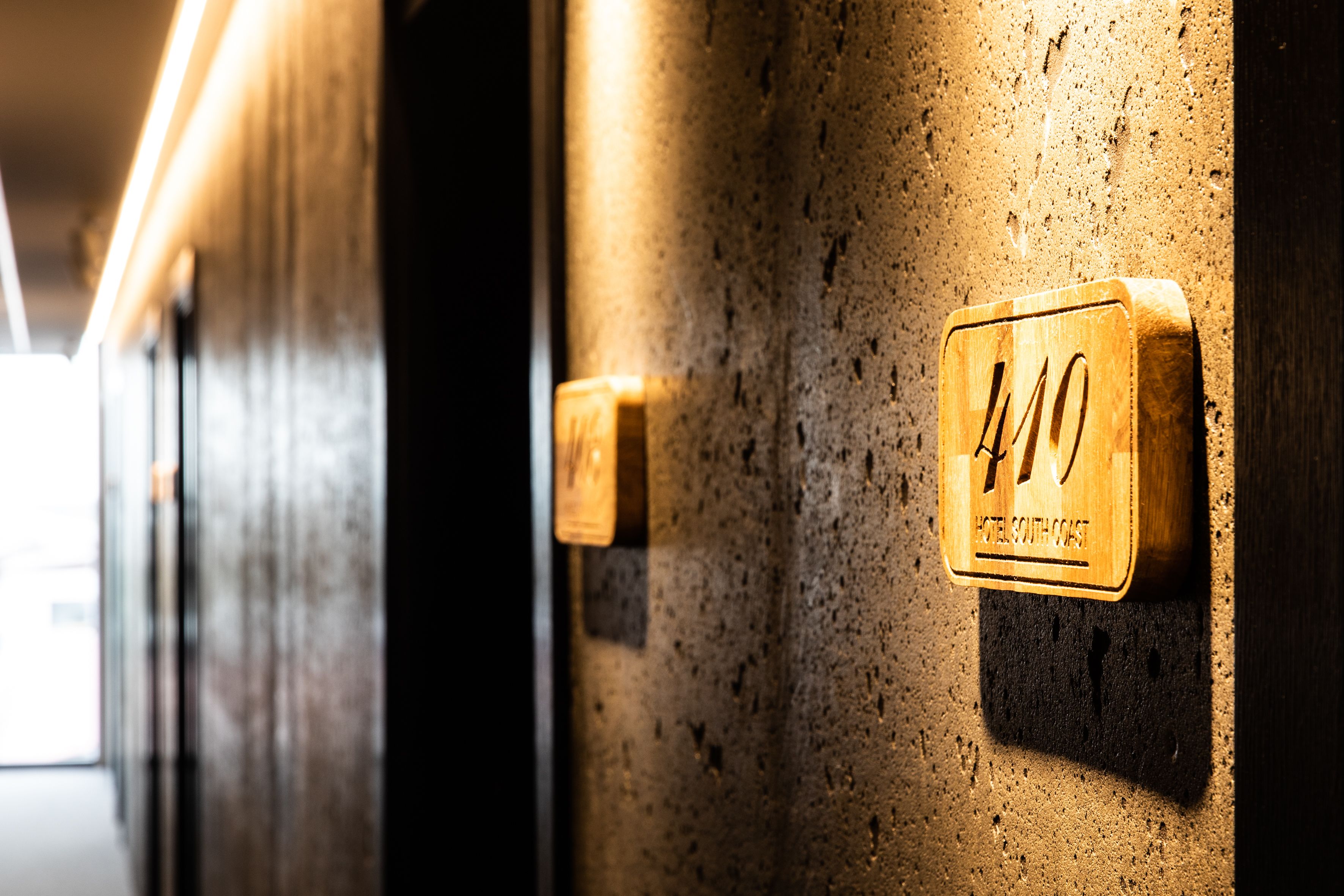 A hotel room with a wooden number plaque, a textured wall, and a door.