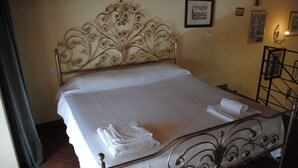 A neatly made bed with a decorative headboard, a folded towel on the bed, and a wall with framed pictures.