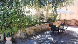 A stone wall with potted plants, a table with chairs, and an umbrella providing shade.