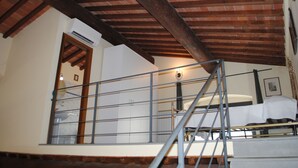 A room with a wooden ceiling, a bed, a window, and a wall-mounted air conditioning unit.