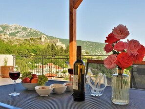 Et bord dækket med vin, frugt og blomster på en balkon med udsigt til et bjerg.