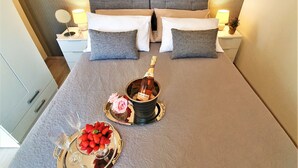 A neatly made bed with a champagne bottle and strawberries on a tray, a bedside table with a lamp, and a patterned wall. - Holiday House Above with pool (Klis)