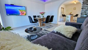 A modern living room with a flat-screen TV, a dining area with chairs, a sofa, and a fluffy white throw. - Holiday House Above with pool (Klis)