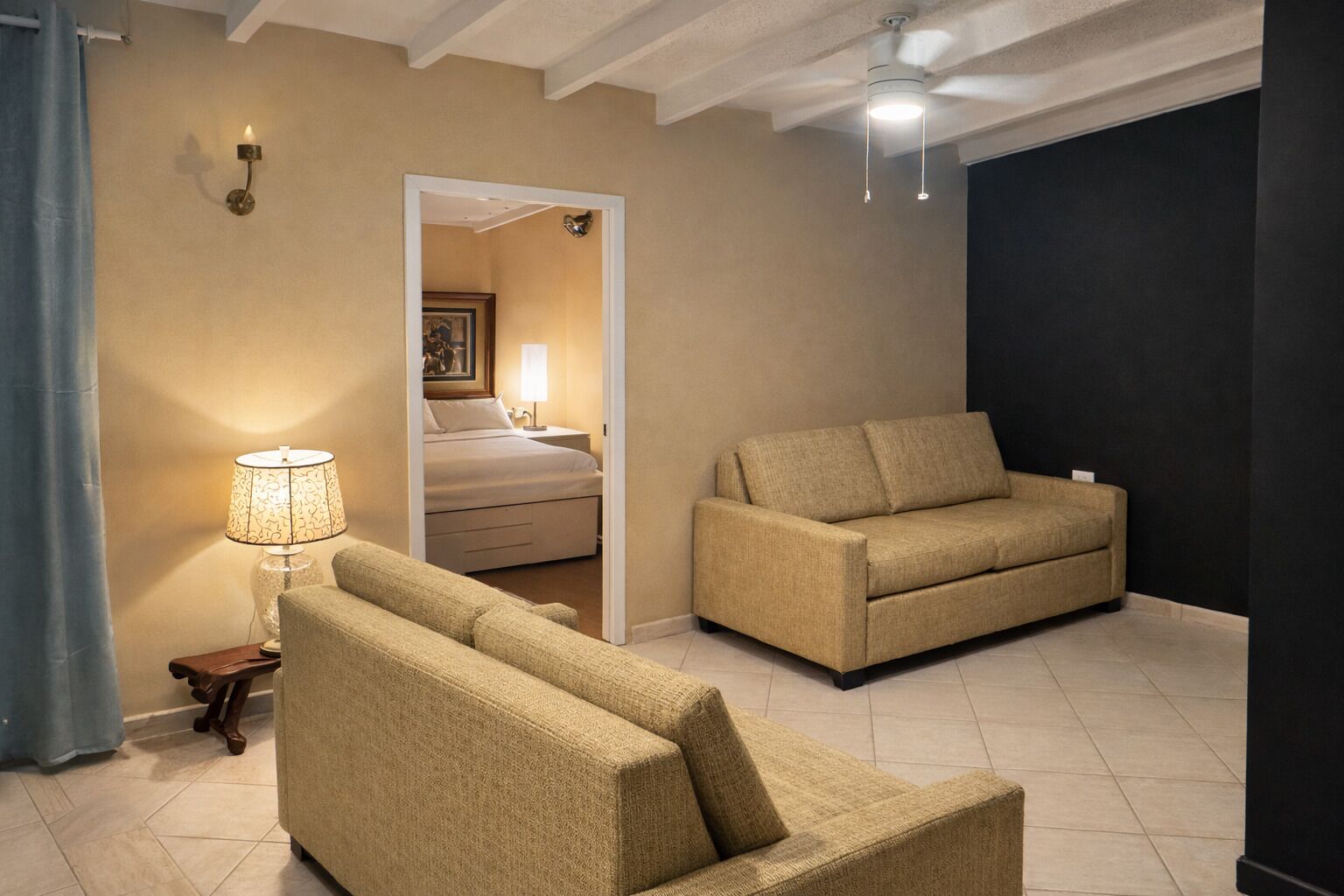 A hotel room with a beige sofa, a smaller armchair, a lamp, and a ceiling fan.