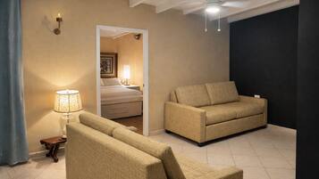 A hotel room with a beige sofa, a smaller armchair, a lamp, and a ceiling fan.