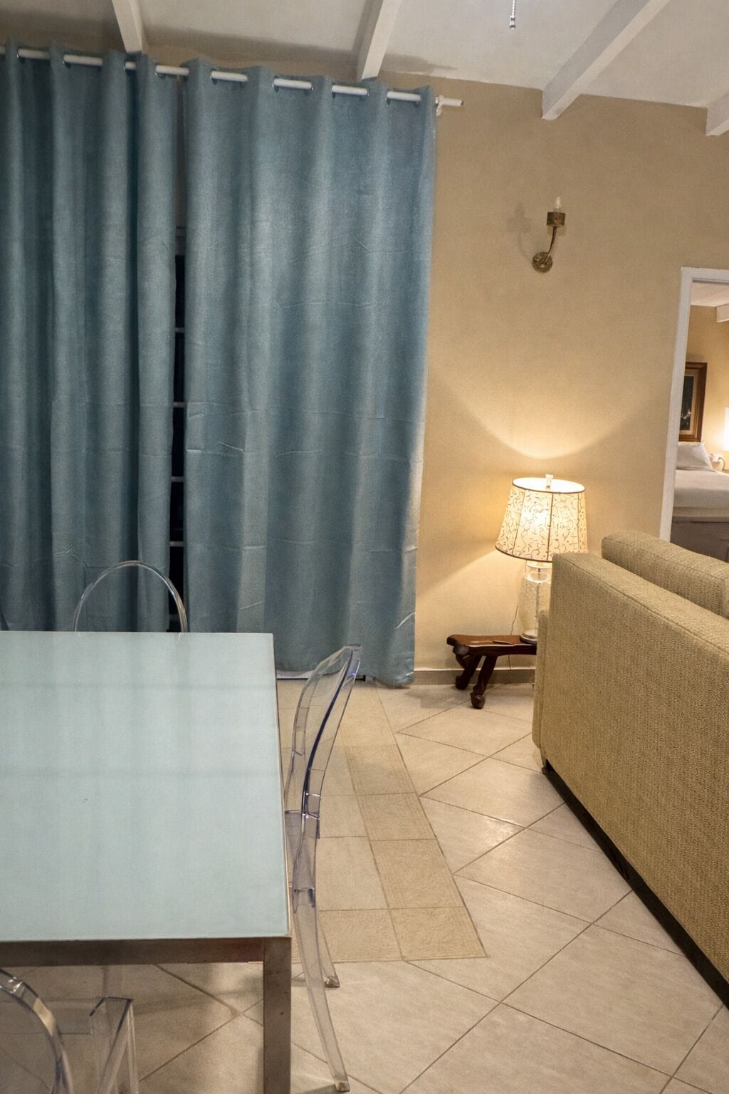 Um quarto com uma mesa de jantar, cadeiras, um sofá, um abajur e uma cortina.