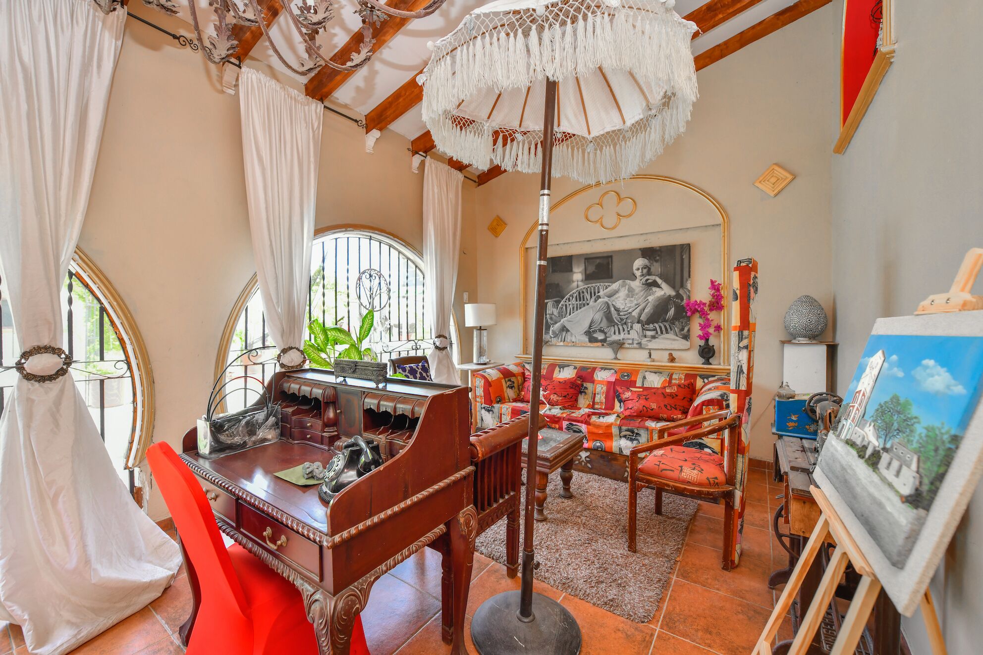 A cozy room with a wooden desk, a red chair, a large mirror, and a ceiling fan.
