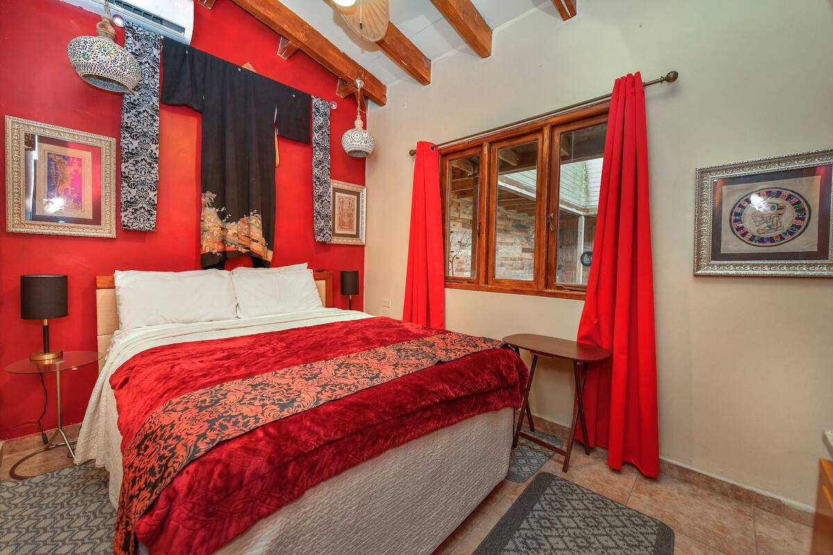 A bedroom with a large bed, red curtains, and a window with a view.