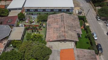 An aerial view of a building with a large flat roof, surrounded by greenery and a parking area.