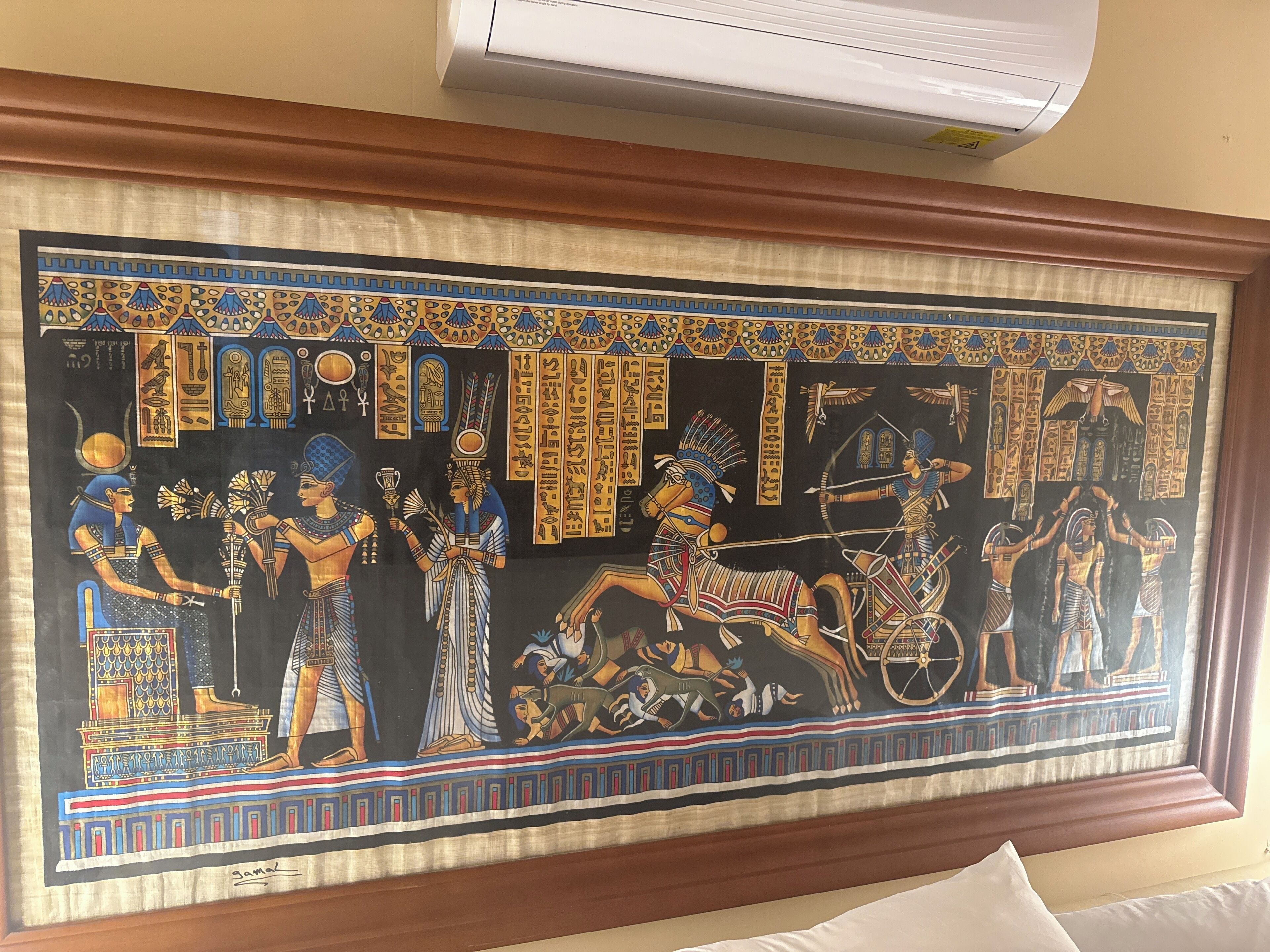 A framed ancient Egyptian painting with hieroglyphics and figures in traditional attire.