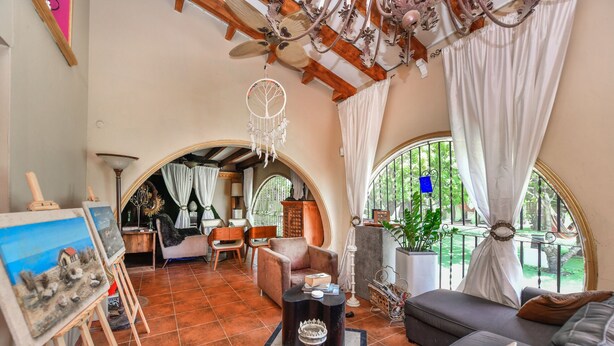 Un amplio salón con un sofá grande, una mesa de centro y un cuadro sobre caballetes. Hay dos sillones, una lámpara y un ventilador de techo decorativo.