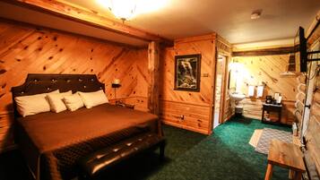 A wooden cabin bedroom with a bed, bench, dresser, and a small table with a lamp.
