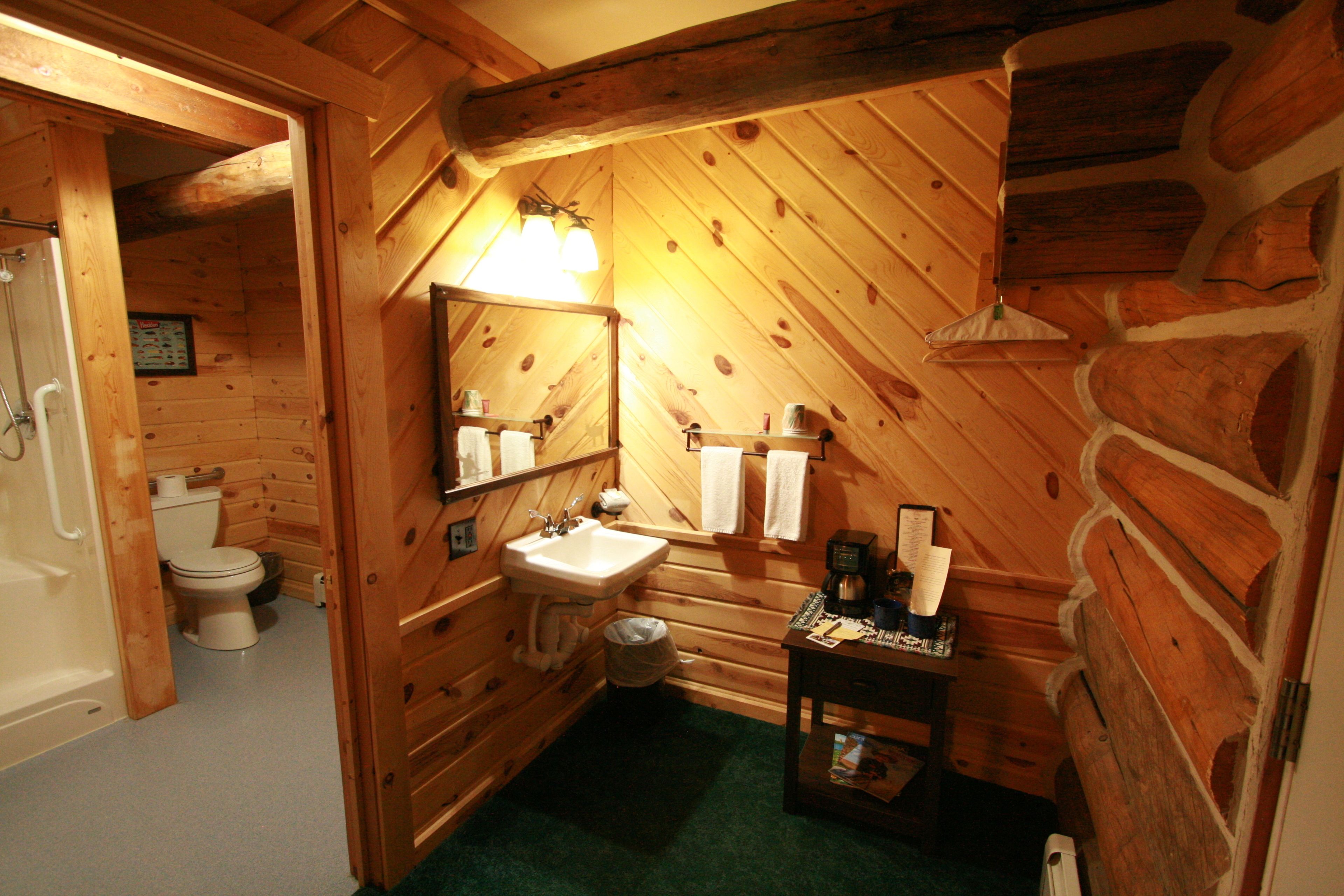 A wooden cabin bathroom with a sink, mirror, and toilet.