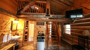 A log cabin interior with a wooden staircase, a sink, a microwave, a television, and a sign reading "Welcome". - Judith Mountain Lodge (Lewistown)