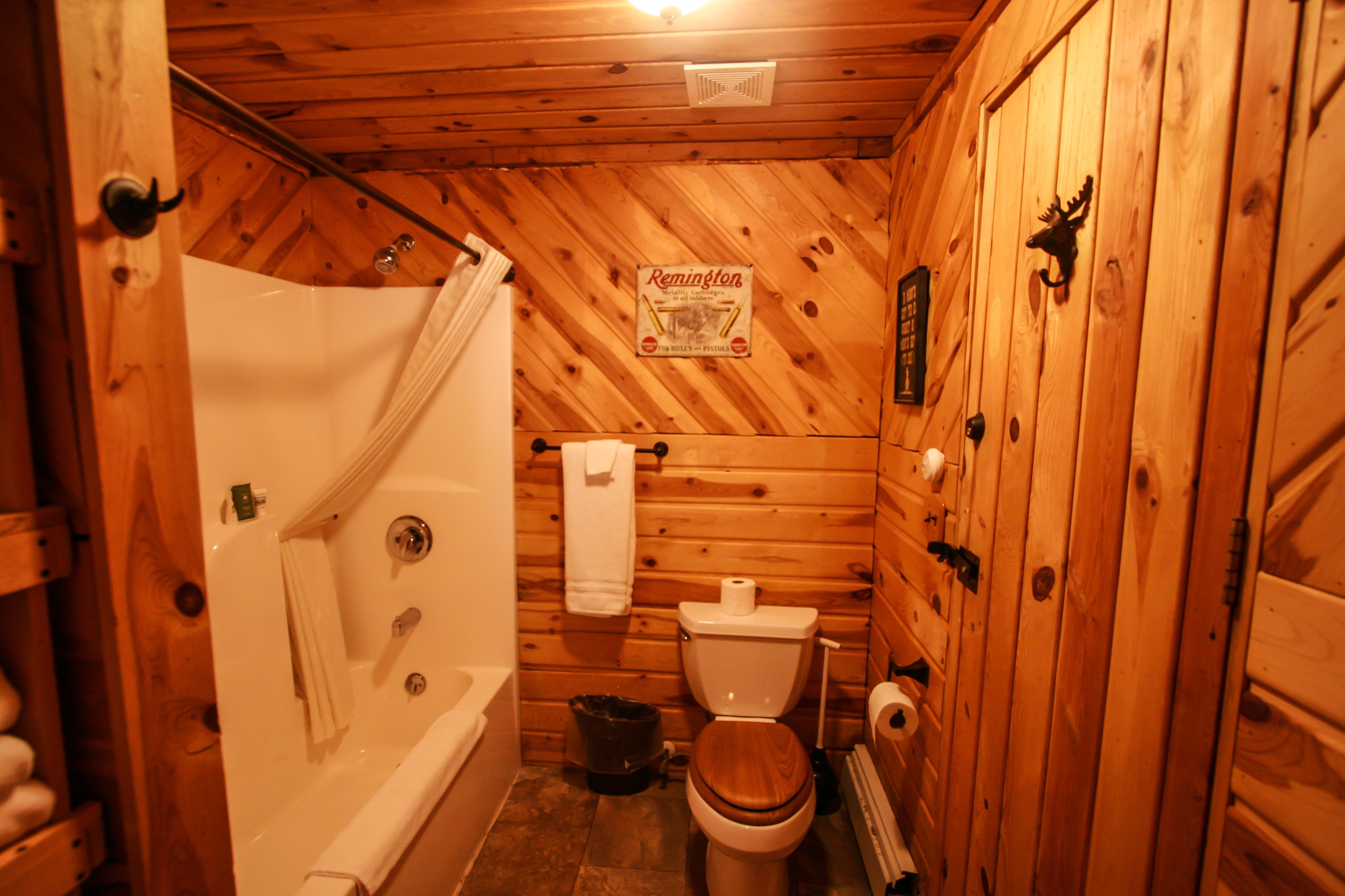 Une salle de bain rustique, avec des murs en bois, comprenant une baignoire, des toilettes et un rideau de douche.