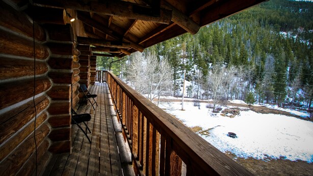 A log cabin with a wooden deck and a view of a snowy landscape. - Judith Mountain Lodge (Lewistown)