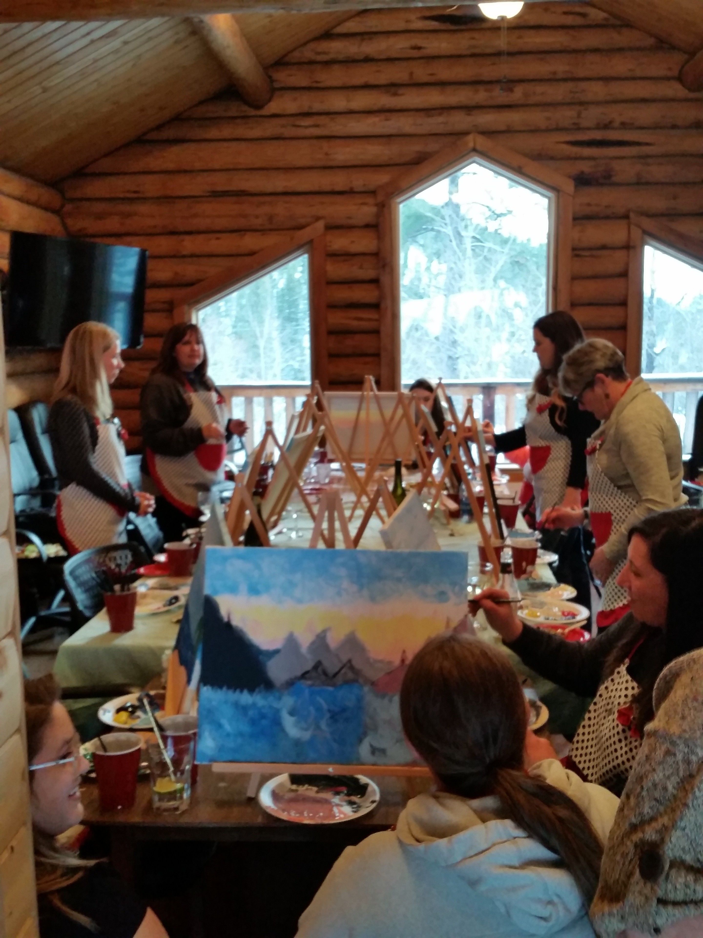 Un grupo de personas pintando en una cabaña rústica con paredes de madera y ventanas amplias.