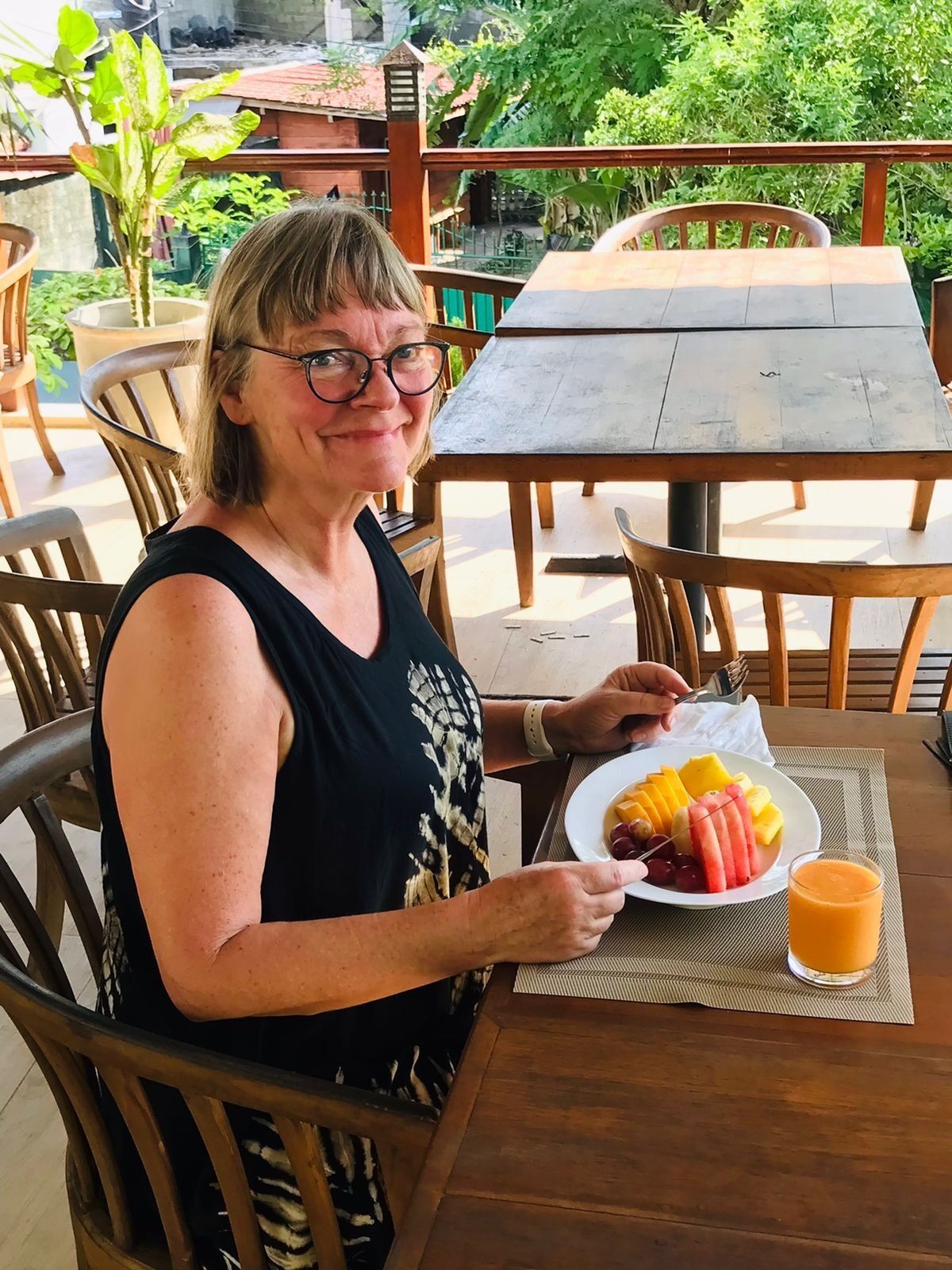 A person seated at an outdoor table with a plate of fruit and a glass of orange juice.