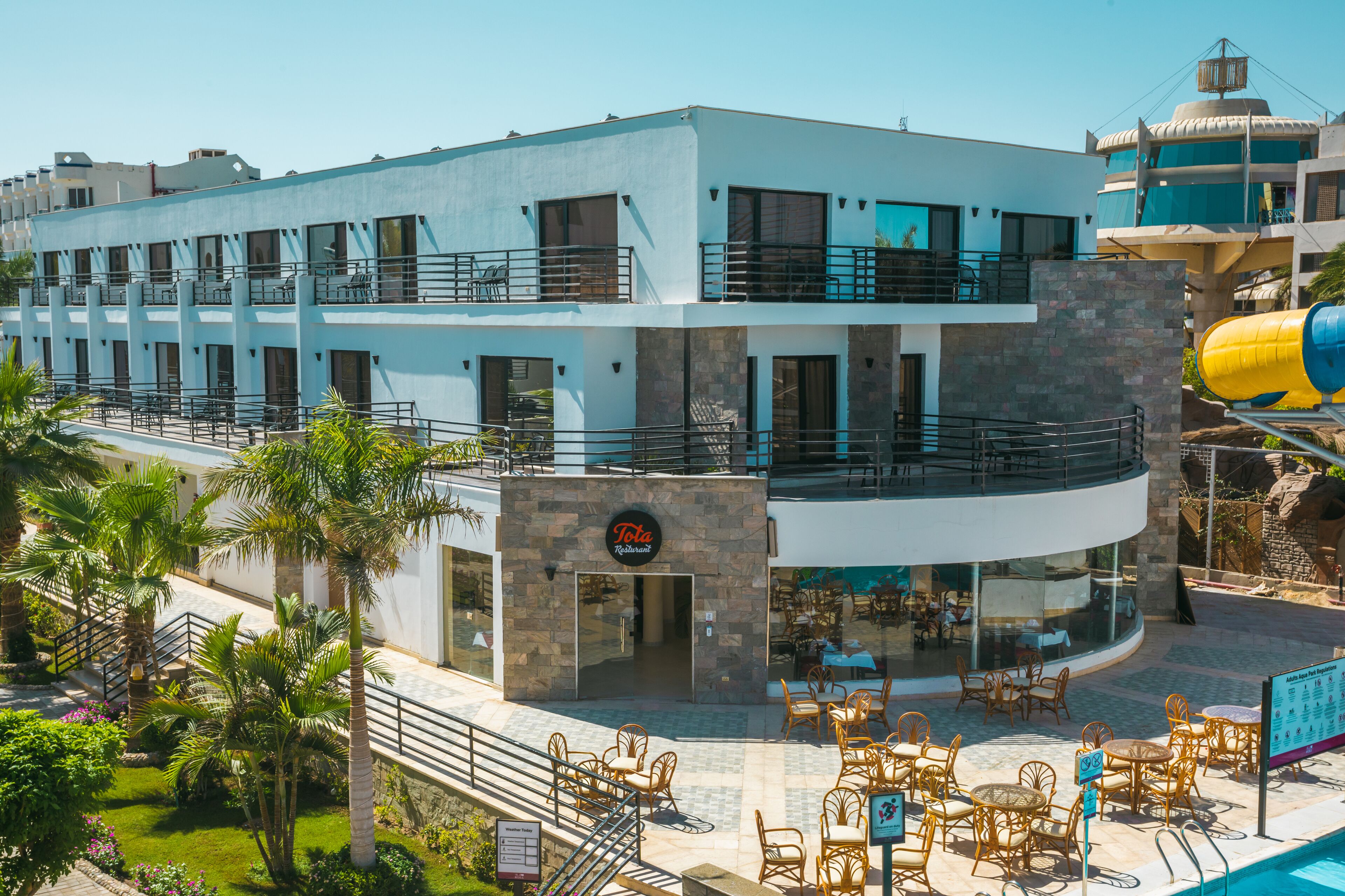 A hotel with a modern design, featuring a pool area with lounge chairs and a water slide.