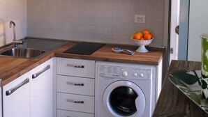 A compact kitchen with white cabinets, a built-in washing machine, a wooden countertop, and a sink. - Welcome to Sicilian Home (Milazzo)