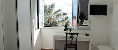 A small, bright room with a desk, chair, and a TV mounted on the wall.