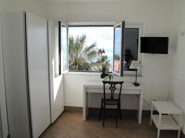 A small, bright room with a desk, chair, and a TV mounted on the wall.
