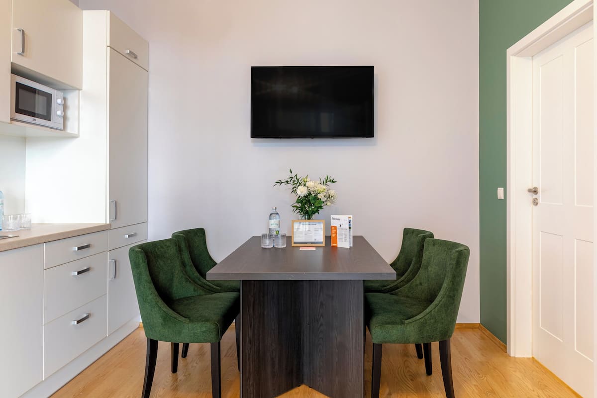 A modern kitchen with white cabinets, a microwave, and a dining table with two green chairs.