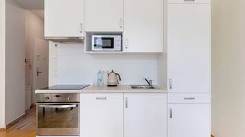 A modern kitchen with white cabinets, a microwave, a kettle, and a sink.