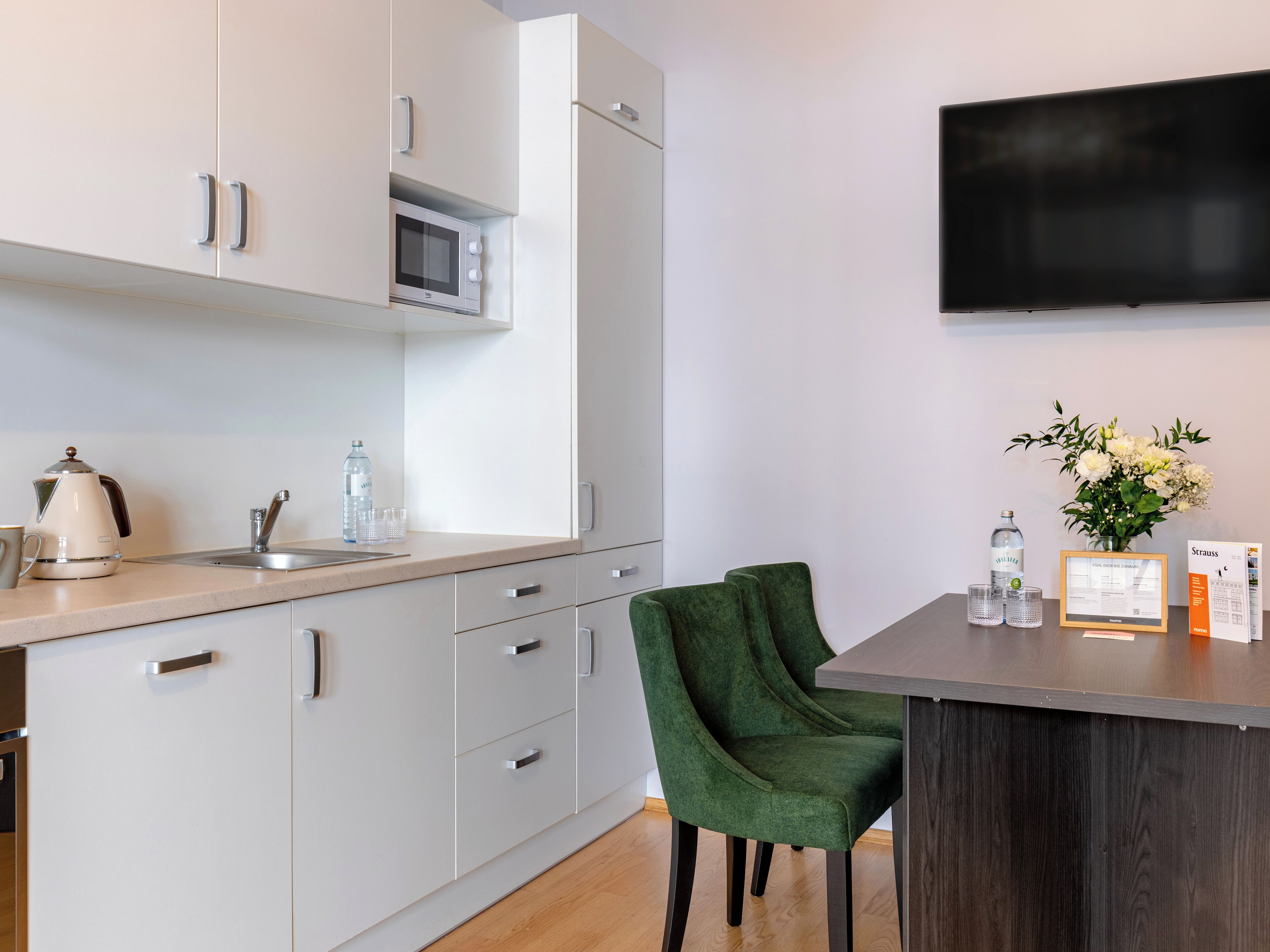 Una cocina moderna con armarios blancos, un microondas, un hervidor y una silla verde.