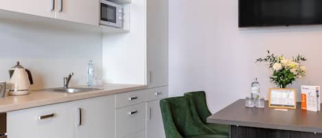 A modern kitchen with white cabinets, a microwave, a kettle, and a green chair.