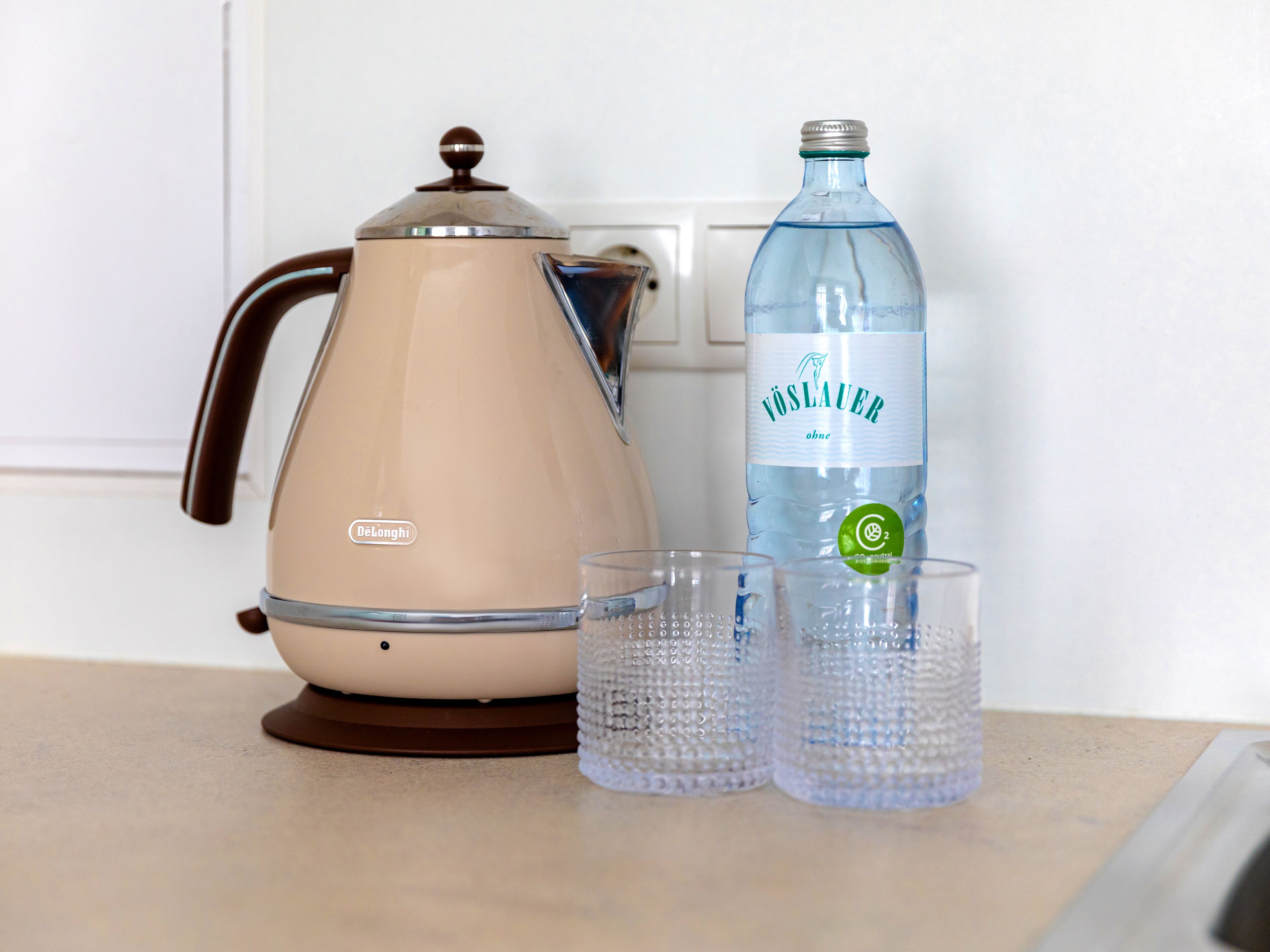 A DeLonghi electric kettle and a bottle of Vosslauer water on a kitchen counter.