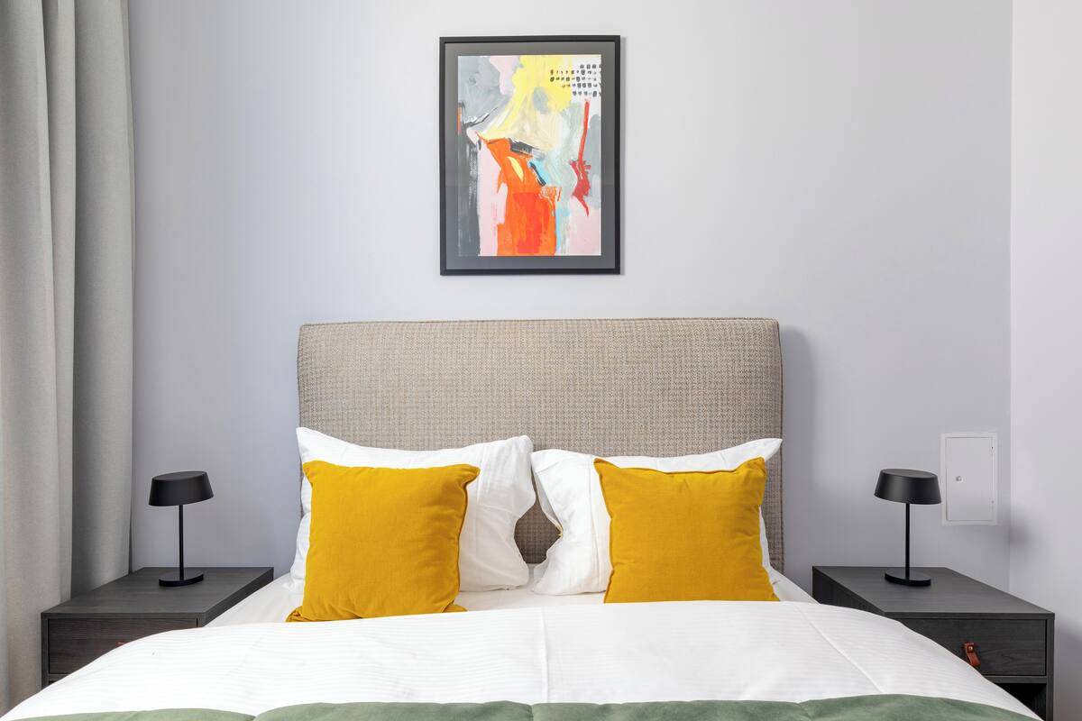 A modern bedroom with a large bed, two bedside tables, and a framed abstract painting on the wall.
