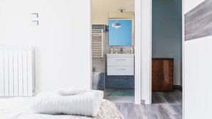 Ein modernes Schlafzimmer mit einem ordentlich bezogenen Bett, ein sichtbares Badezimmer mit Handtuchhalter und eine Holztür, die in einen anderen Raum führt.