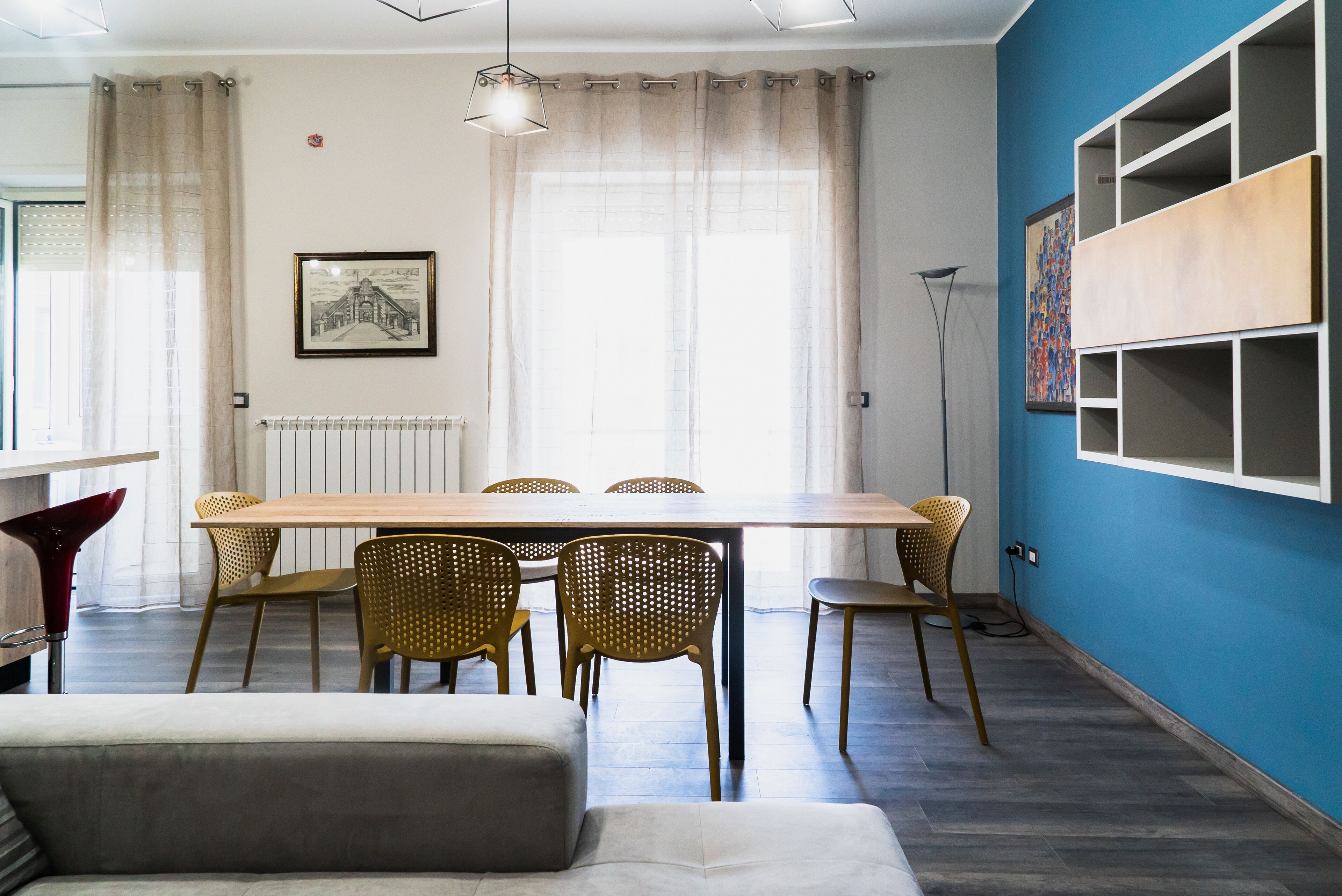 Ein Essbereich mit Holztisch und Korbstühlen, einer Couch und einem Heizkörper an der Wand.