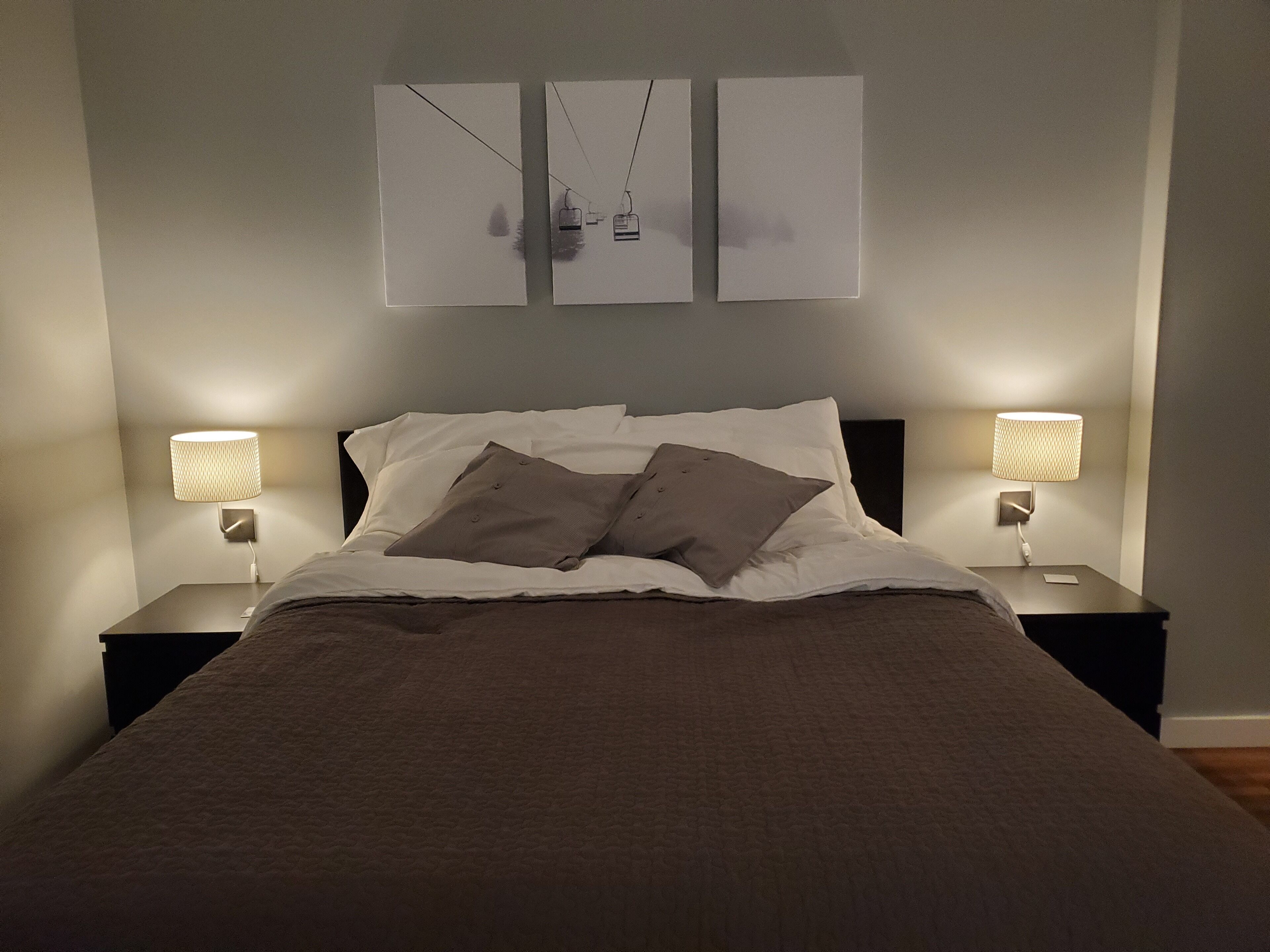 A neatly made bed with a brown blanket and pillows, two bedside lamps, and a wall-mounted picture above the bed.