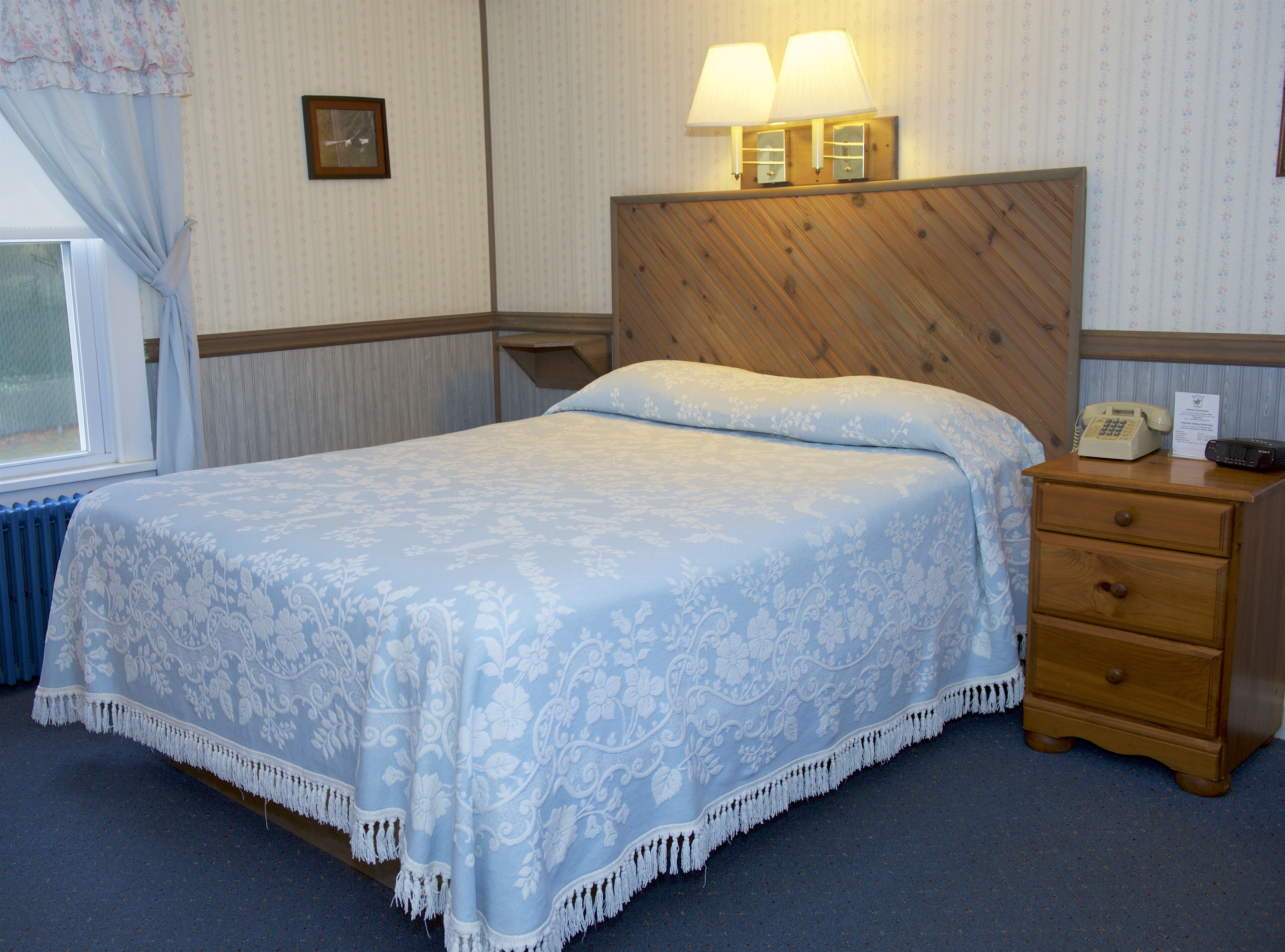 A hotel room with a bed, a nightstand with a telephone, and a wall-mounted lamp.
