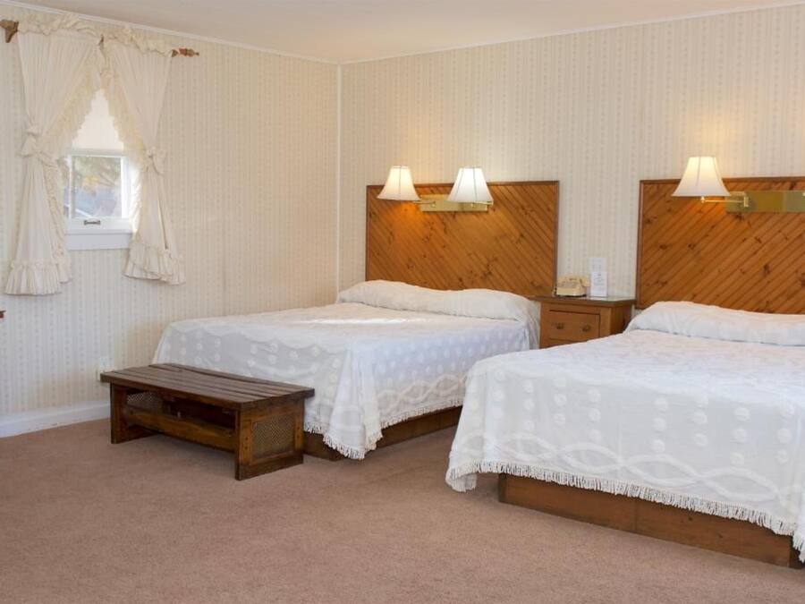 Une chambre d’hôtel avec deux lits, une tête de lit en bois, un bureau avec une chaise, un petit banc en bois et un miroir.