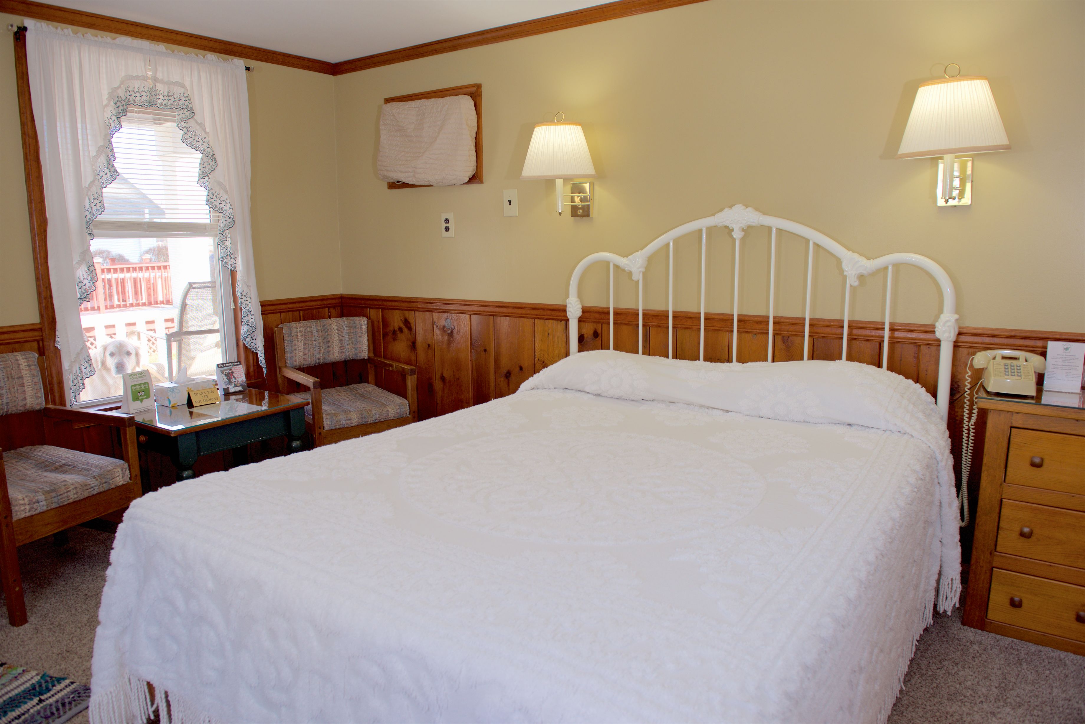 A neatly arranged bedroom with a single bed, a bedside table, a chair, and two wall-mounted lamps.