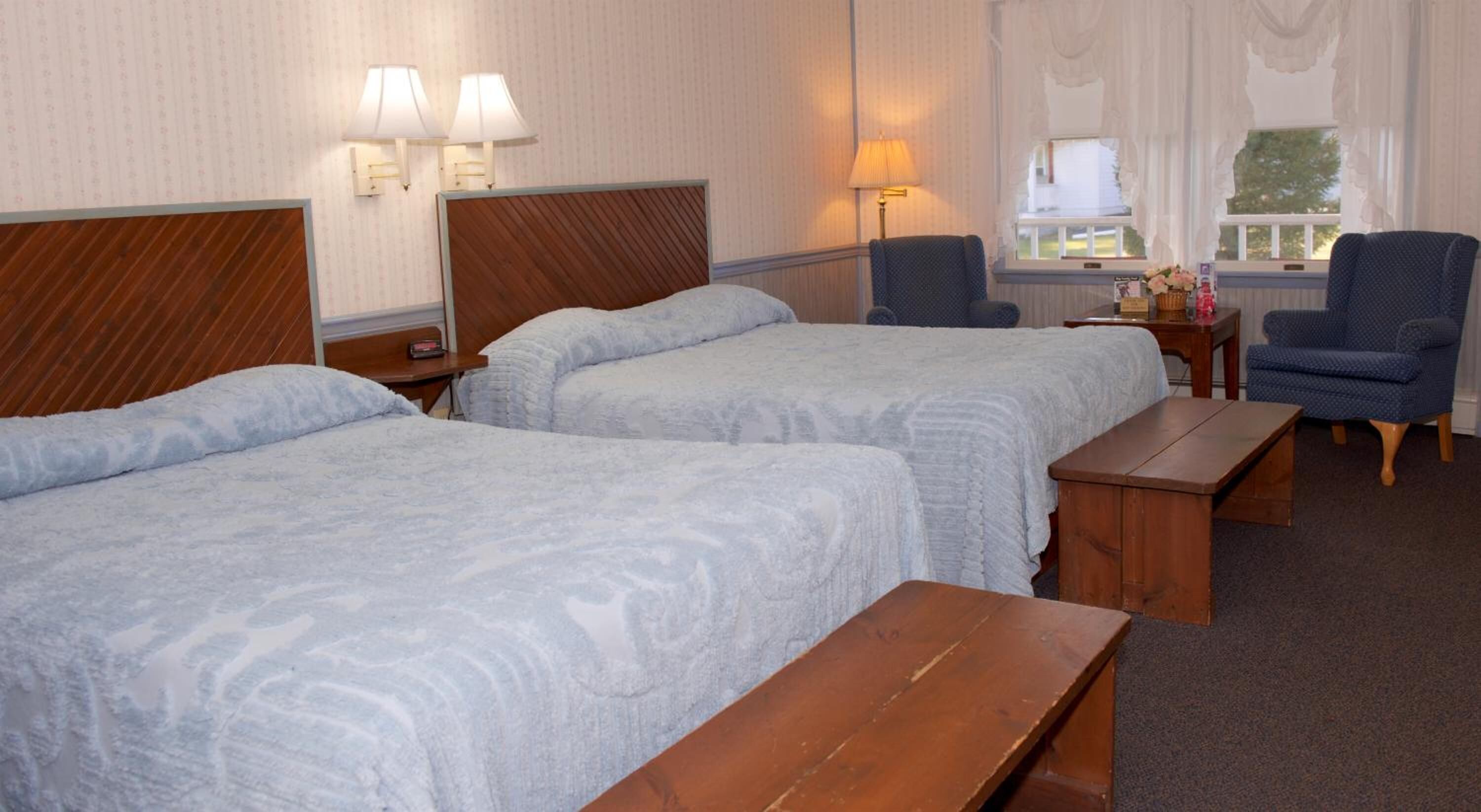 Ein Hotelzimmer mit zwei Betten, einer hölzernen Bank, einem Schreibtisch, zwei Stühlen und einem Fenster mit Blick.