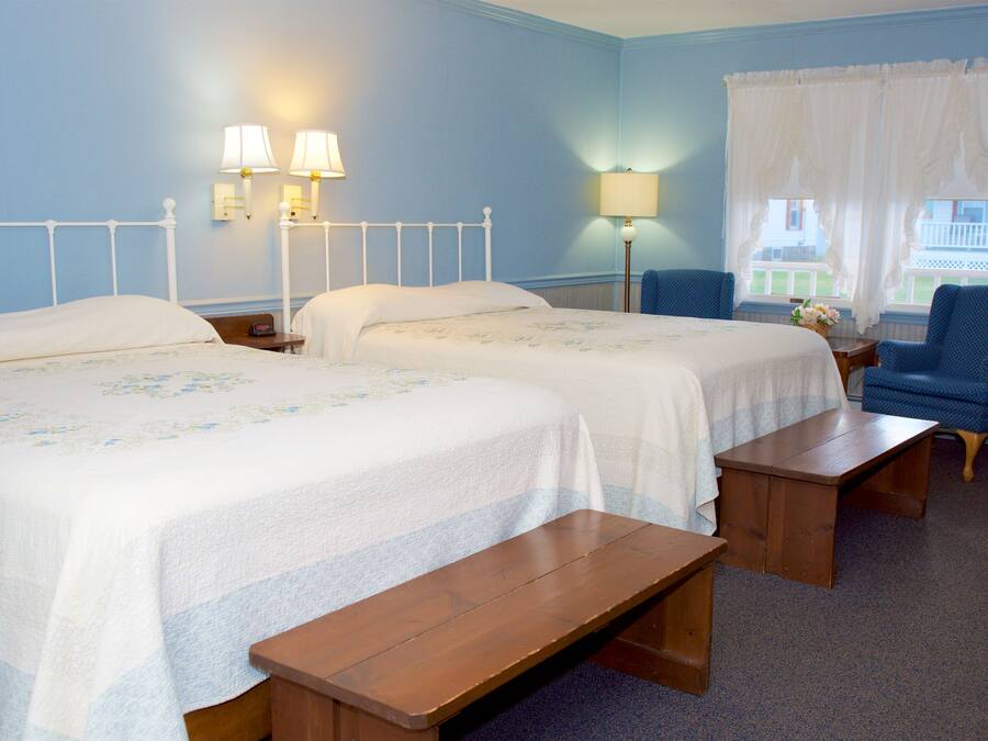 Habitación de hotel con dos camas, una silla, una mesa y dos lámparas de pared.