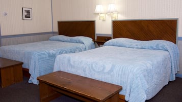 Una habitación de hotel con dos camas individuales, un banco de madera y una mesita de noche con lámpara.