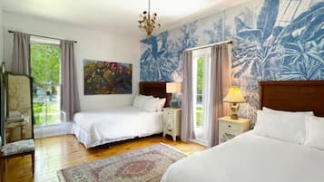 Un dormitorio con dos camas, un ventanal grande, una araña y un mural tropical.