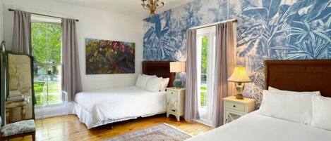 A bedroom with two beds, a large window, a chandelier, and a tropical mural.
