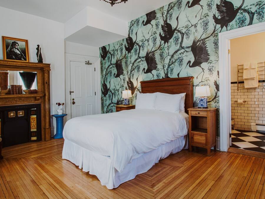 A bedroom with a large bed, wooden floor, a dresser with a mirror, and a wall with a bird mural.