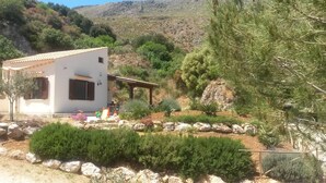 Un edificio blanco con tejado de tejas, rodeado de un jardín con diversas plantas y una pérgola.