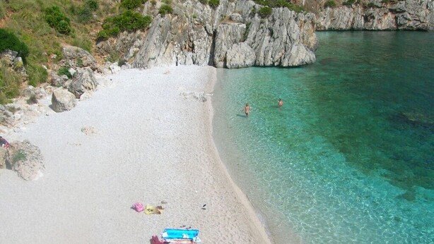 Una playa con aguas turquesas cristalinas, acantilados rocosos y algunas personas nadando.