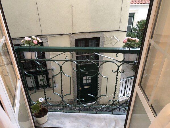 A balcony with a metal railing, potted plants, and a view of the street below.