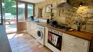 A kitchen with stone walls, a washing machine, and a large window overlooking a pool area. - Stunning Provence Hilltop Salazac Farmhouse with views, private pool and air con (Salazac)