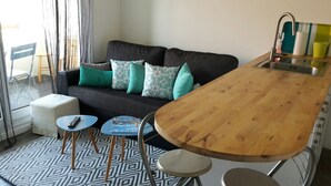A compact living space with a sofa, a small table, a stool, and a kitchenette area. - T2 apartment near beach, swimming pool, tennis (Bidart)